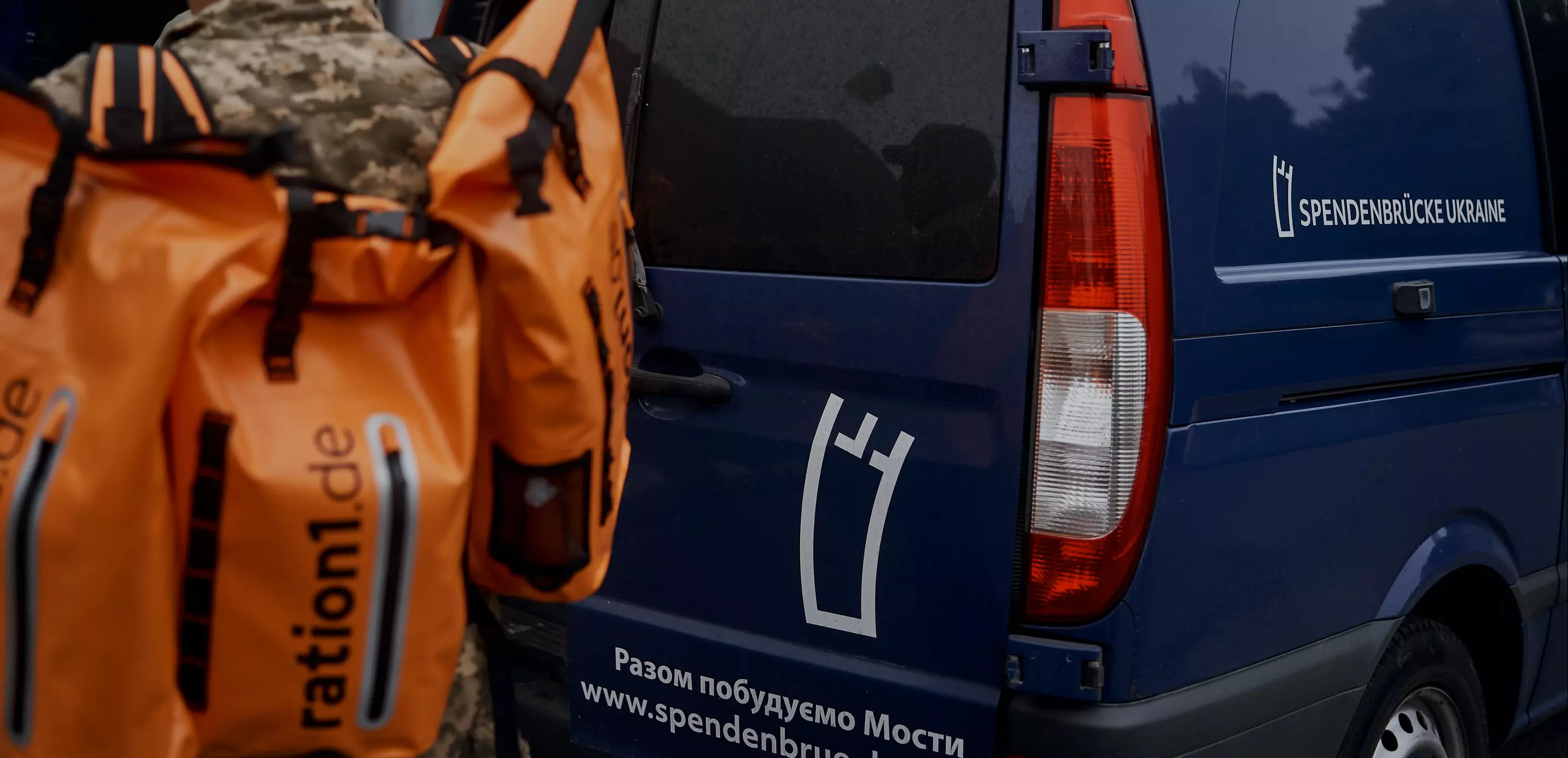 Hilfsgüter in orangefarbenen Taschen vor einem dunkelblauen Transporter mit dem Aufdruck 